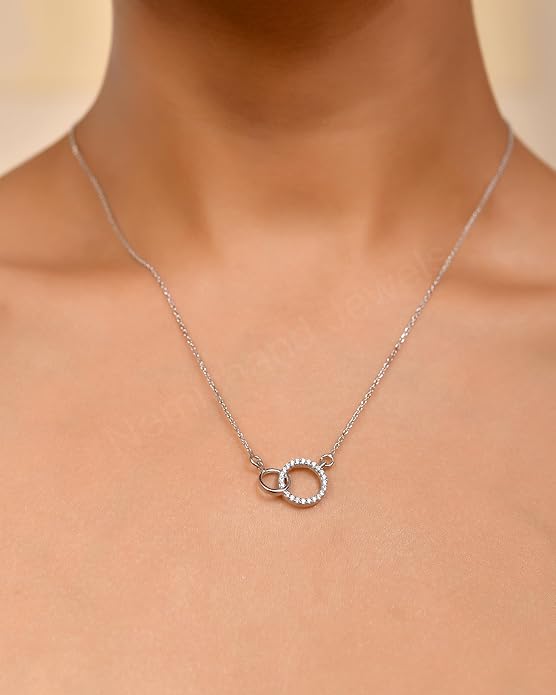 Silver necklace with a circular pendant on a person's neck against a neutral background