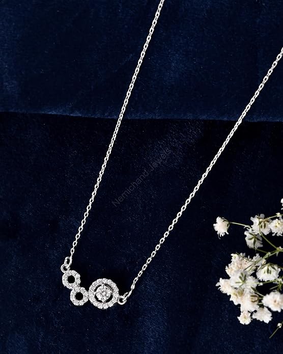 Silver necklace with circular design on a dark blue background with white flowers.