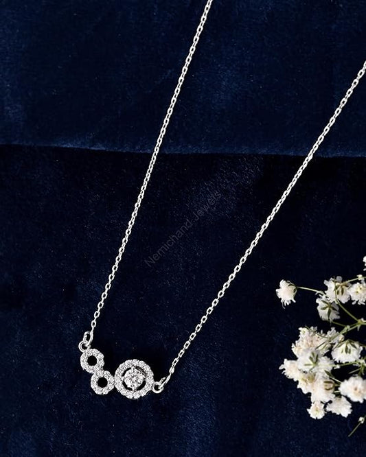 Silver necklace with circular design on a dark blue background with white flowers.